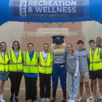 staff volunteers posing with Louie the Laker in front of an inflatable arch.